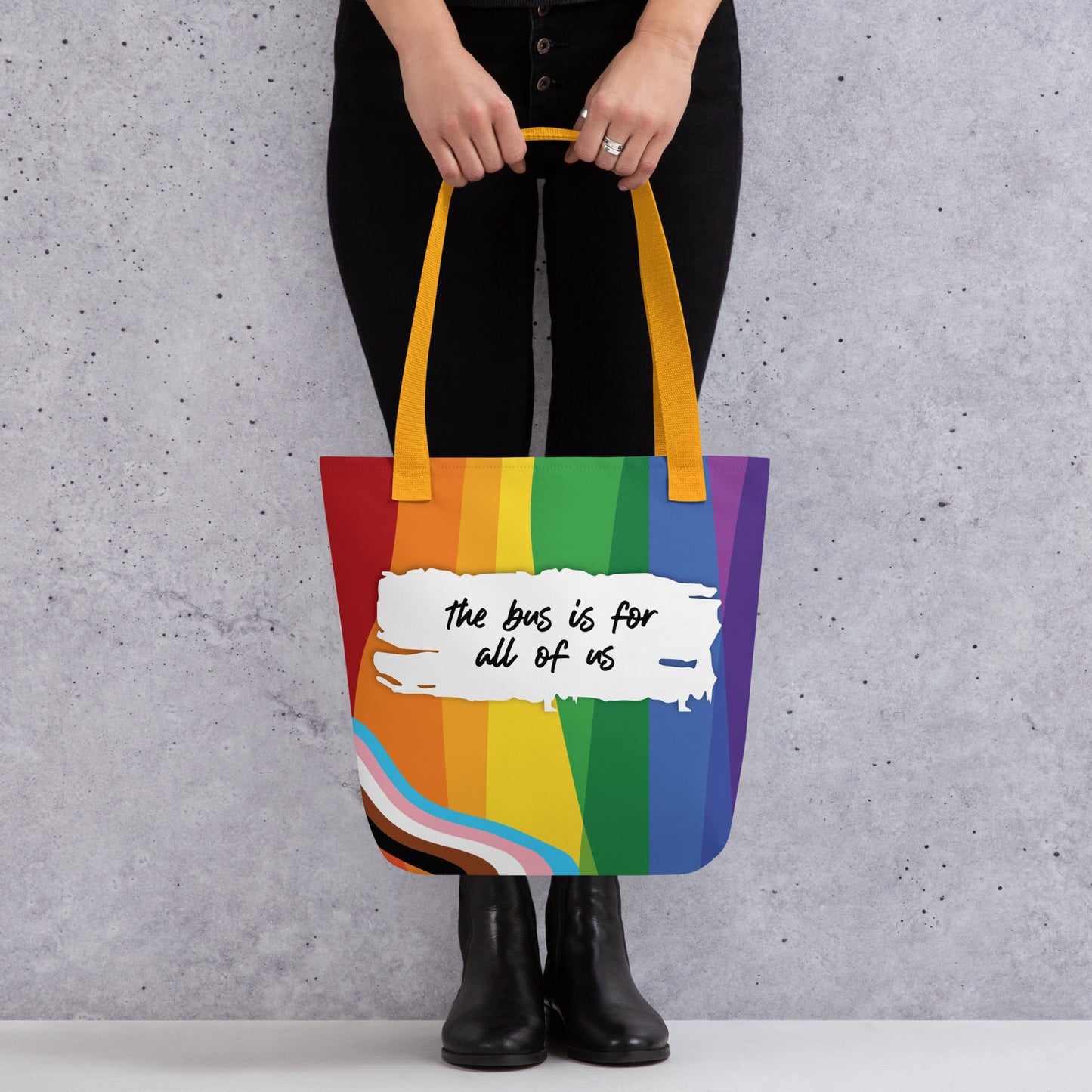 Person holding a rainbow tote bag with text against a gray background